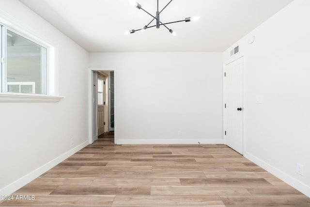 unfurnished room featuring light wood-type flooring and an inviting chandelier