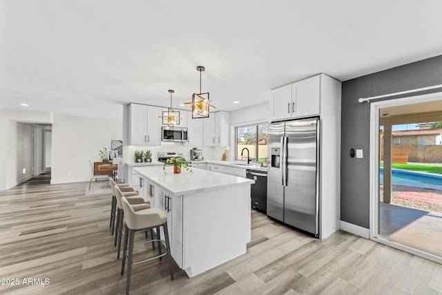 kitchen with stainless steel appliances, white cabinetry, a center island, and decorative light fixtures