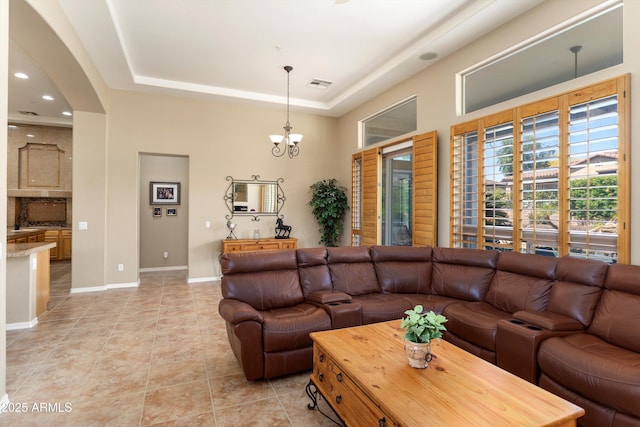 12976 W Plum Rd, Peoria, AZ 85383 - living room with a raised ceiling, baseboards, arched walkways, light tile patterned flooring, and a notable chandelier