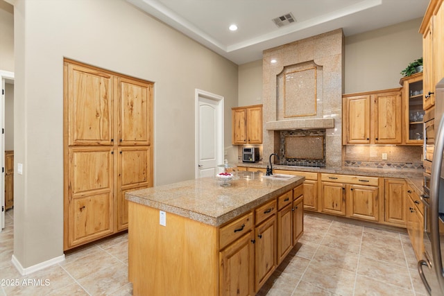 12976 W Plum Rd, Peoria, AZ 85383 - kitchen featuring decorative backsplash, a sink, visible vents, a tray ceiling, and a center island with sink