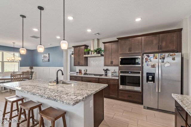 4514 W Hazel Ln, San Tan Valley, AZ 85144 - kitchen with stainless steel appliances, a sink, wall chimney exhaust hood, dark brown cabinetry, and a breakfast bar area