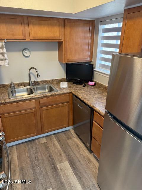 kitchen with stainless steel fridge, black dishwasher, sink, and light hardwood / wood-style flooring