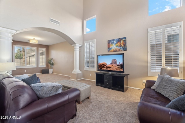 living room featuring a towering ceiling, light colored carpet, and ornate columns