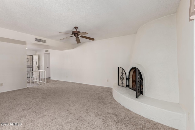 unfurnished living room with a textured ceiling, ceiling fan, visible vents, and carpet