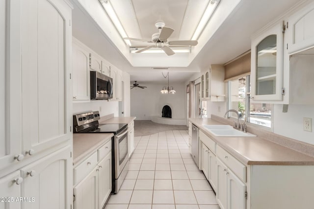 kitchen with a ceiling fan, a sink, light tile patterned floors, a fireplace with raised hearth, and stainless steel appliances