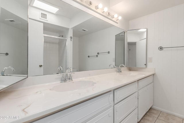 bathroom featuring a shower with shower door, double vanity, a sink, and tile patterned flooring