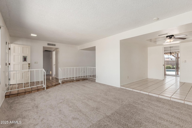 carpeted empty room with visible vents, a ceiling fan, and a textured ceiling