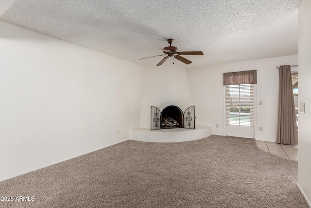 unfurnished living room featuring carpet floors, a textured ceiling, ceiling fan, and a large fireplace