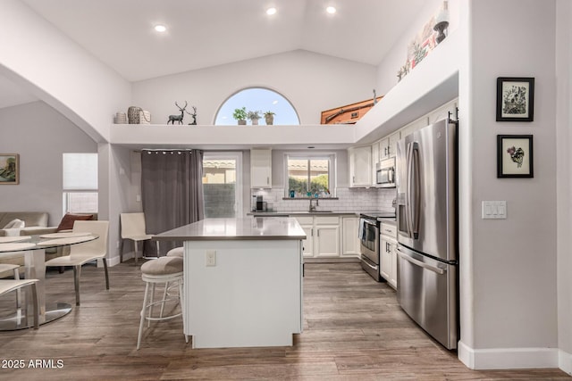 kitchen with white cabinets, appliances with stainless steel finishes, a kitchen island, backsplash, and a breakfast bar