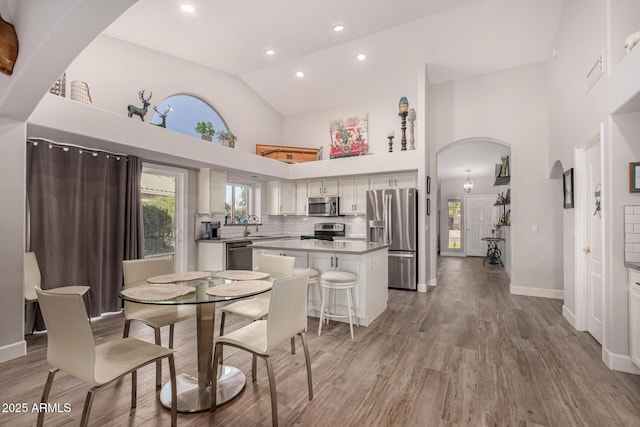 dining area featuring sink, light hardwood / wood-style floors, and high vaulted ceiling