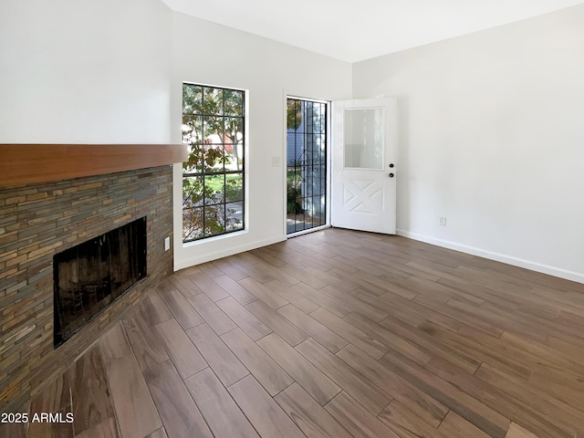 unfurnished living room featuring dark hardwood / wood-style floors, a stone fireplace, and a wealth of natural light