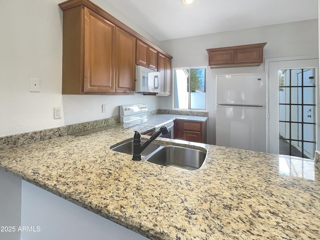 kitchen featuring kitchen peninsula, white appliances, light stone counters, and sink