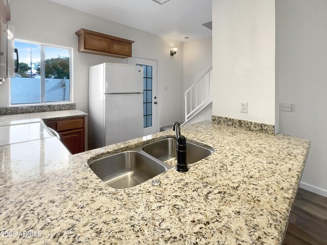 kitchen with kitchen peninsula, white refrigerator, light stone counters, and sink