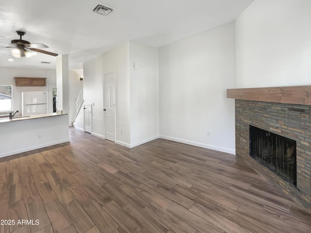 unfurnished living room featuring dark hardwood / wood-style floors, a stone fireplace, ceiling fan, and sink