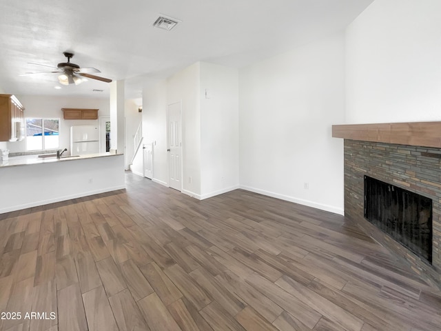 unfurnished living room featuring a stone fireplace, ceiling fan, dark hardwood / wood-style flooring, and sink