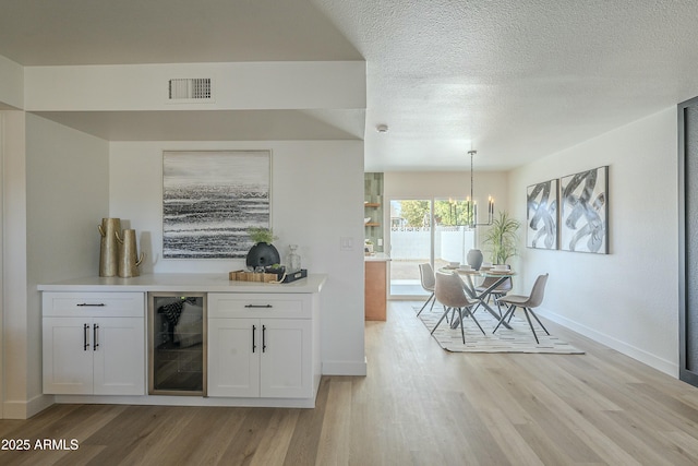 bar featuring pendant lighting, a textured ceiling, white cabinets, beverage cooler, and light wood-type flooring