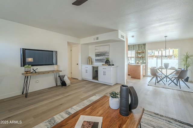 living room featuring wine cooler, light hardwood / wood-style flooring, a textured ceiling, and an inviting chandelier