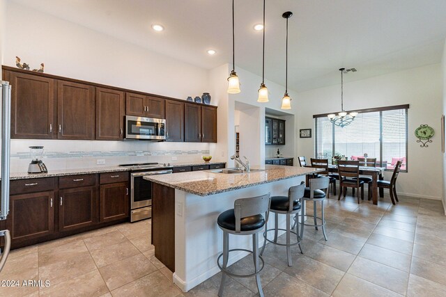 kitchen featuring light stone countertops, stainless steel appliances, a chandelier, and a center island with sink