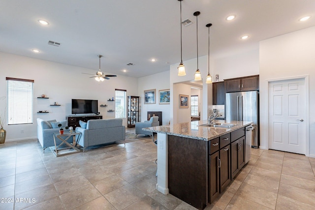 kitchen with decorative light fixtures, light stone counters, an island with sink, sink, and ceiling fan