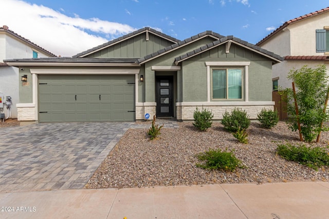 view of front of house with a garage, a tile roof, stone siding, decorative driveway, and stucco siding