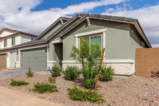 view of front of home with stone siding, fence, decorative driveway, and stucco siding