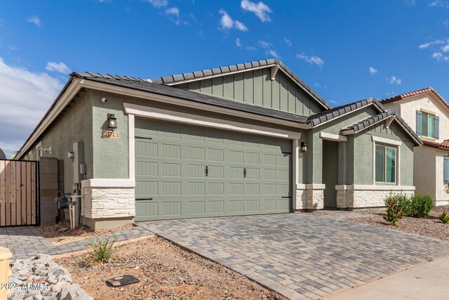 view of front of house with a garage, stone siding, a gate, decorative driveway, and stucco siding