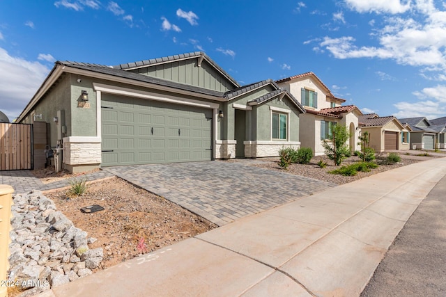 view of front facade featuring a garage, stone siding, a gate, decorative driveway, and stucco siding