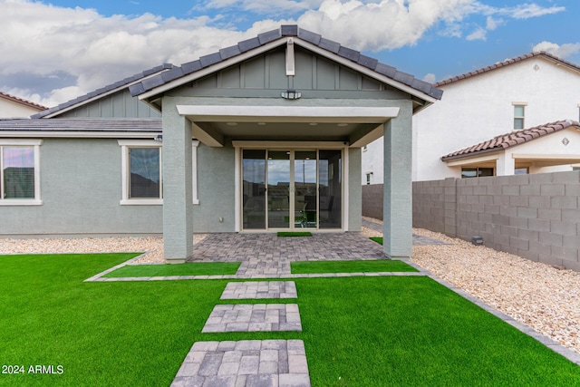 back of property featuring fence, a lawn, stucco siding, board and batten siding, and a patio area