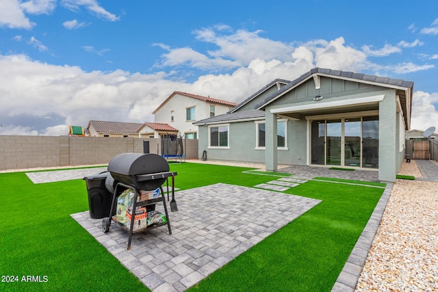 rear view of house with a trampoline, a yard, a patio, stucco siding, and a fenced backyard