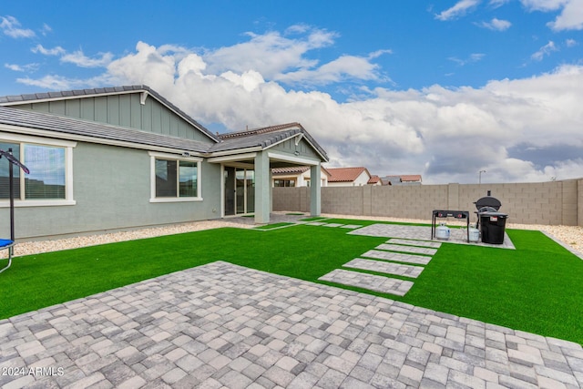 back of property with a patio, a lawn, a fenced backyard, and board and batten siding