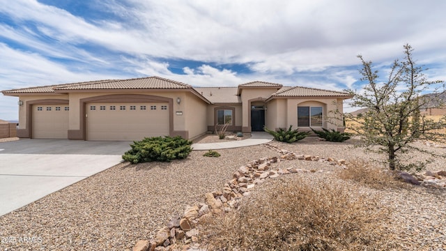 mediterranean / spanish home featuring stucco siding, an attached garage, a tile roof, and driveway