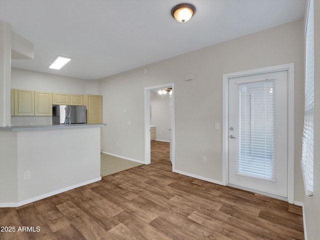 kitchen featuring light wood-type flooring, cream cabinets, freestanding refrigerator, light countertops, and baseboards