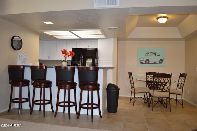 kitchen featuring dark countertops, visible vents, black refrigerator with ice dispenser, white cabinets, and a kitchen breakfast bar