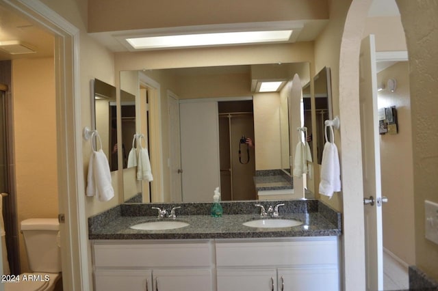 full bathroom with toilet, double vanity, and a sink