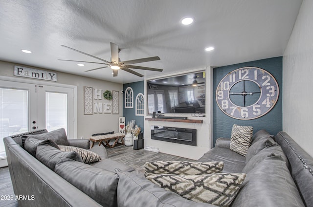 living room featuring a glass covered fireplace, wood finished floors, a textured ceiling, french doors, and recessed lighting