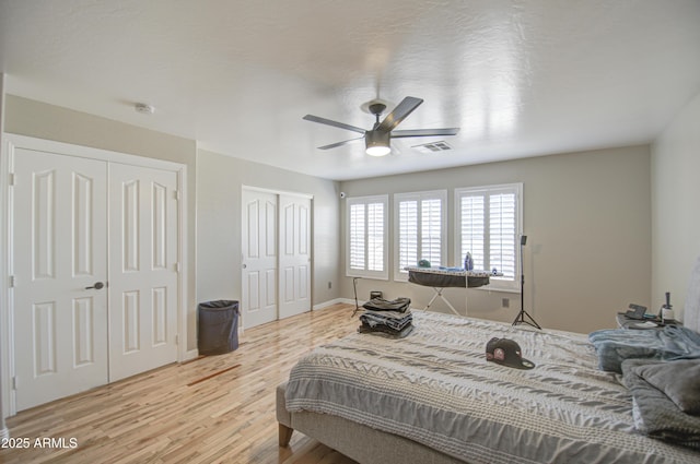 bedroom featuring ceiling fan, visible vents, light wood-style floors, baseboards, and multiple closets