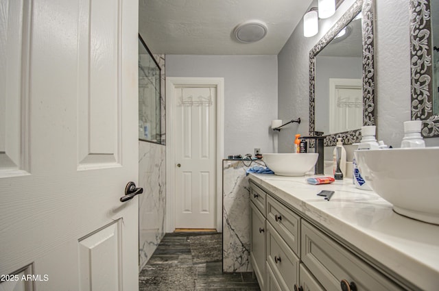 full bathroom with a textured wall, double vanity, wood finished floors, and a sink