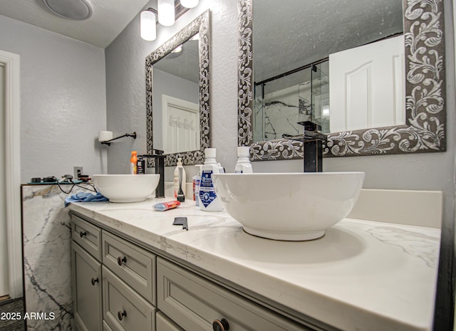 bathroom with a textured wall, double vanity, a stall shower, and a sink