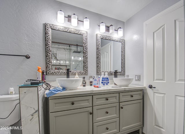 full bathroom with a textured wall, double vanity, a sink, and a shower stall