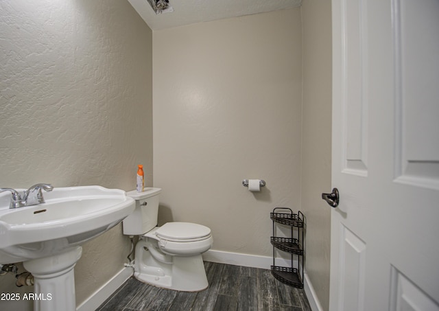 bathroom with baseboards, a textured wall, toilet, and wood finished floors