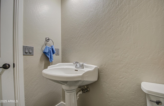 half bath featuring a textured wall and toilet