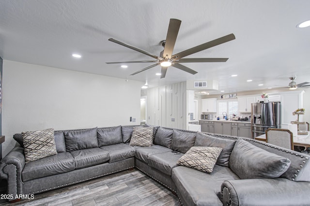 living room featuring light wood-type flooring, ceiling fan, visible vents, and recessed lighting