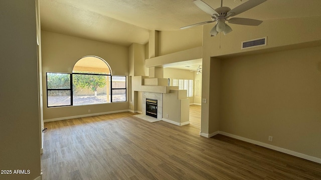 unfurnished living room featuring ceiling fan, a tile fireplace, high vaulted ceiling, and wood-type flooring