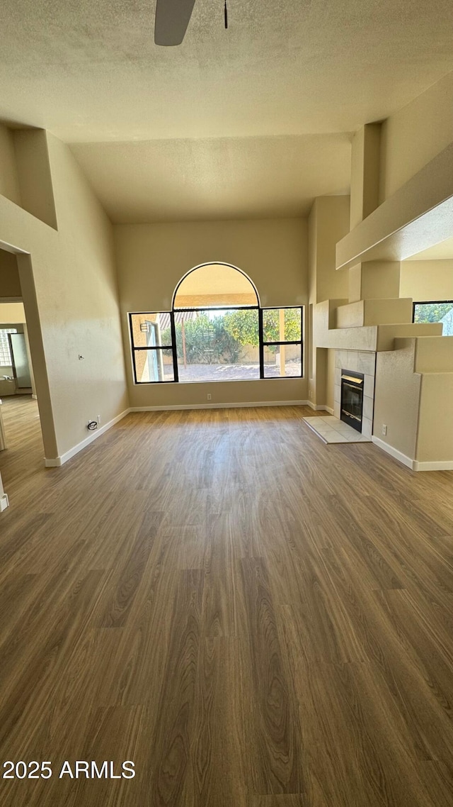 unfurnished living room with ceiling fan, a textured ceiling, a fireplace, and wood-type flooring