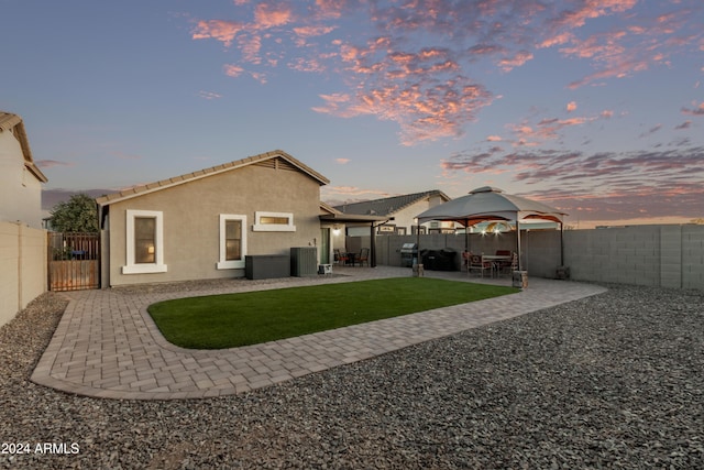 back house at dusk with a gazebo, a patio, and central AC unit