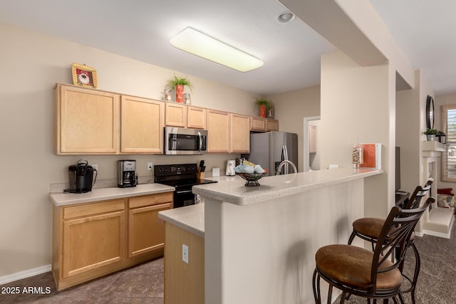 kitchen featuring light brown cabinets, stainless steel appliances, a kitchen bar, and light countertops