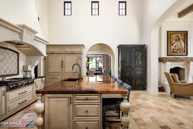 kitchen with wood counters, stainless steel gas cooktop, sink, a high ceiling, and an island with sink