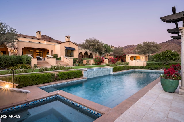 pool at dusk featuring an in ground hot tub