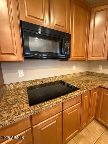 kitchen with light tile patterned flooring, light stone countertops, and black appliances