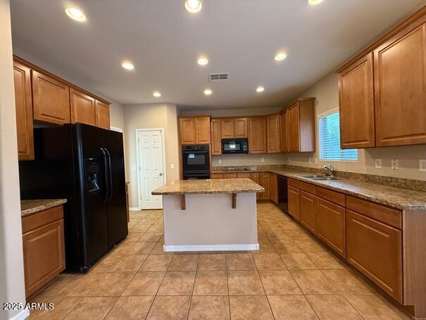 kitchen featuring sink, a kitchen breakfast bar, a center island, black appliances, and light stone countertops